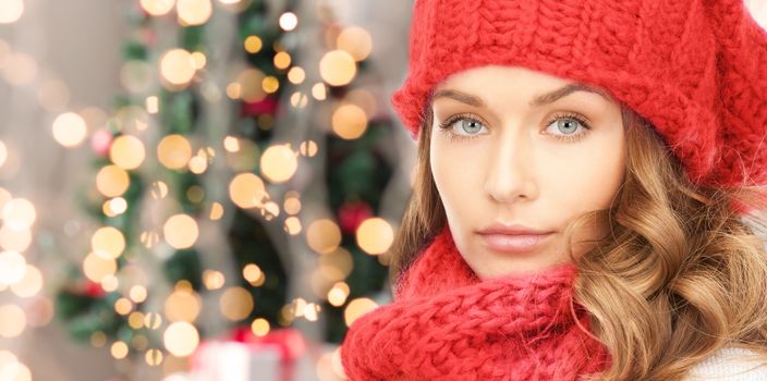 happiness, winter holidays and people concept - close up of young woman in red hat and scarf over christmas tree lights background