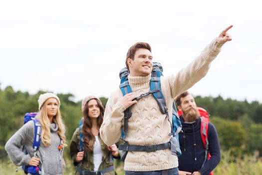 adventure, travel, tourism, hike and people concept - group of smiling friends with backpacks pointing finger outdoors