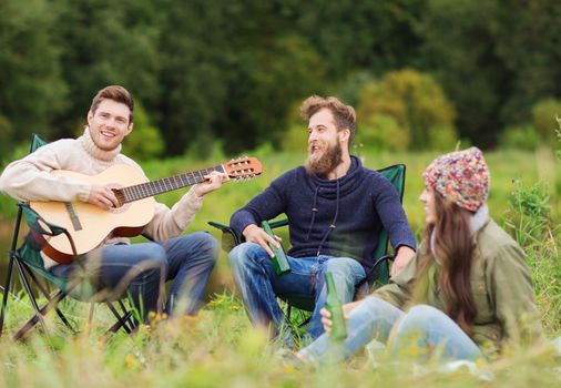 adventure, travel, tourism and people concept - group of smiling tourists playing guitar and drinking beer in camping