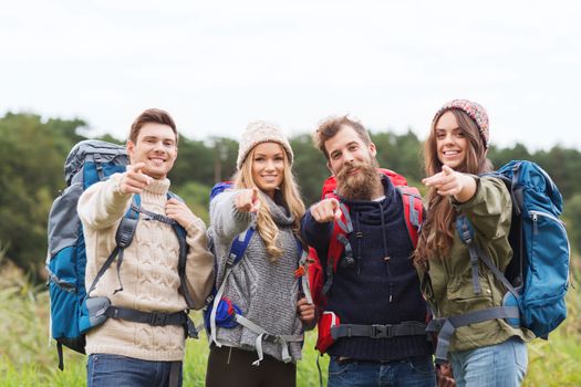 adventure, travel, tourism, hike and people concept - group of smiling friends with backpacks pointing finger outdoors