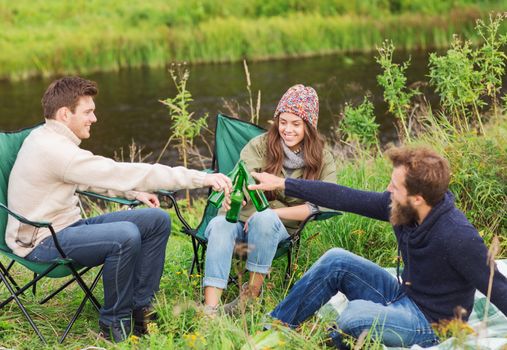 adventure, travel, tourism, friendship and people concept - group of smiling tourists clinking beer bottles in camping