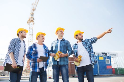 business, building, teamwork, technology and people concept - group of smiling builders in hardhats with tablet pc computer and clipboard outdoors