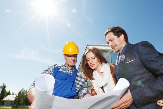 Foreman shows house design plans to a young couple outdoors