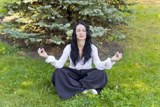 European brunette woman on green grass in yoga pose