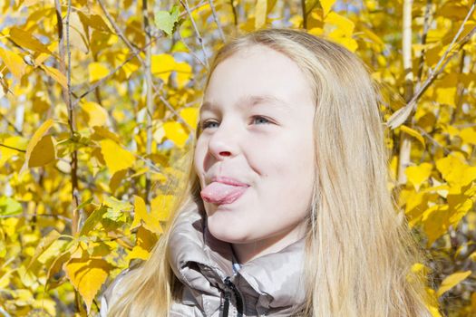 Autumn portrait of blond girl in sunlight put out tongue