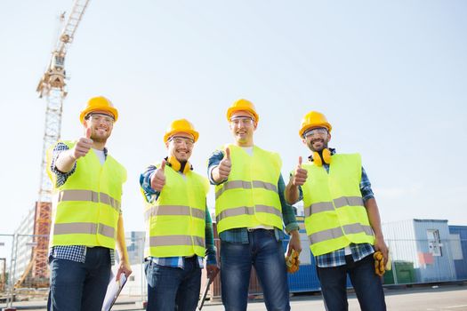 business, building, teamwork, technology and people concept - group of smiling builders in hardhats with tablet pc computer and clipboard showing thumbs up gesture outdoors