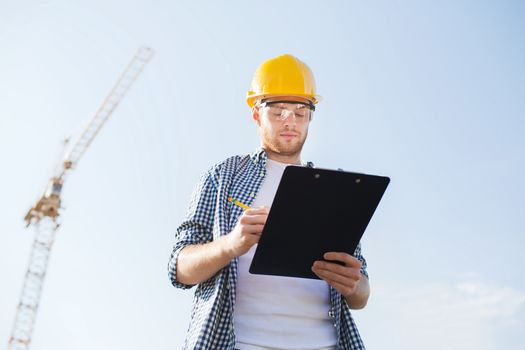 business, building, paperwork and people concept - builder in hardhat with clipboard outdoors