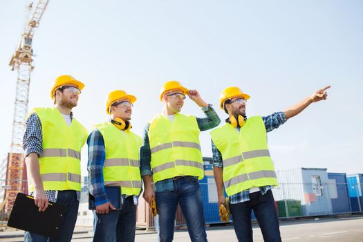 business, building, teamwork, technology and people concept - group of smiling builders in hardhats with tablet pc computer and clipboard outdoors