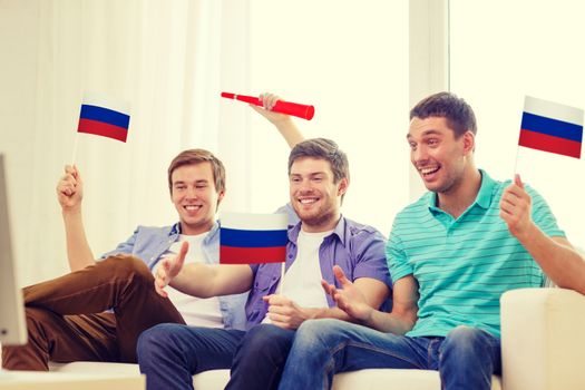 friendship, sports and entertainment concept - happy male friends with flags and vuvuzela supporting football team at home