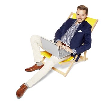 Cheerful man sitting on a sunbed and working on a computer. Isolated on white background. 