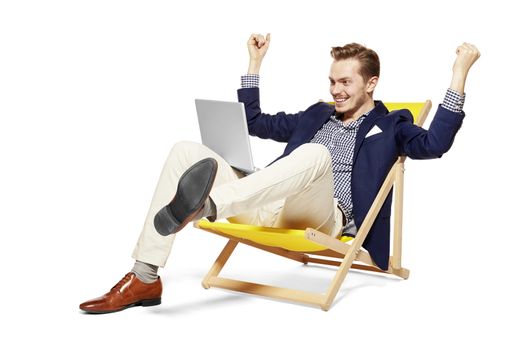 Studio shot of happy young man sitting on sunbed. He raises his arms in a gesture of victory.