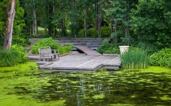 Wood fishing dock over green pond in summer.