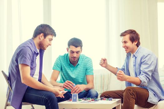 leisure, games and lifestyle concept - happy three male friends playing poker at home