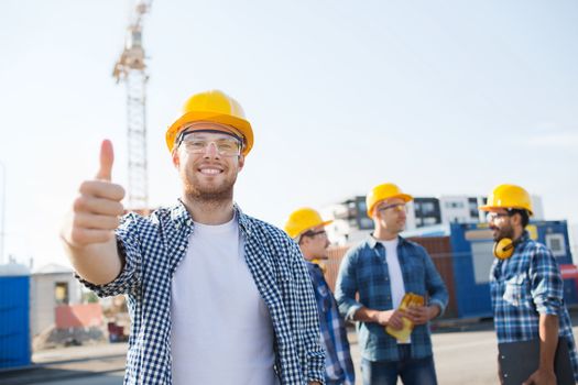 business, building, teamwork, gesture and people concept - group of smiling builders in hardhats showing thumbs up outdoors