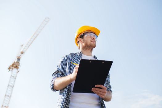 business, building, paperwork and people concept - builder in hardhat with clipboard outdoors