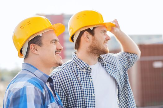 business, building, teamwork and people concept - group of smiling builders in hardhats with clipboard outdoors