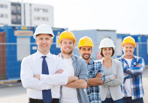 business, building, teamwork and people concept - group of smiling builders in hardhats outdoors