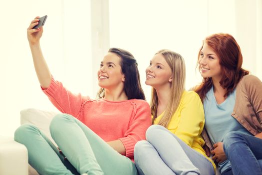 friendship, technology and internet concept - three smiling teenage girls taking selfie with smartphone camera at home