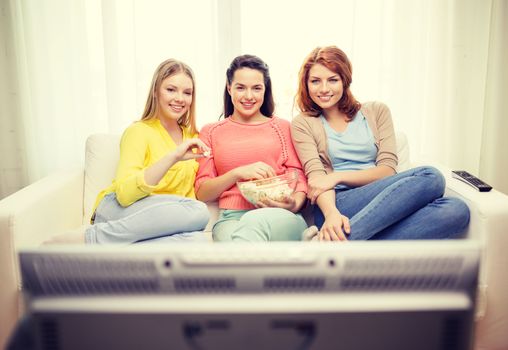 home, technology and friendship concept - three smiling teenage girl watching tv at home and eating popcorn