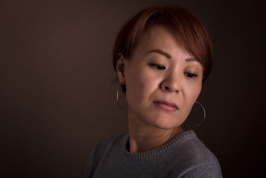 A headshot of a sad looking middle aged Japanese woman.