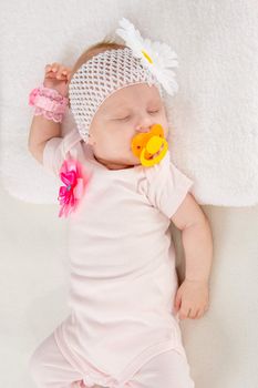 a two-month baby girl Europeans on the back with a bandage on his head with a flower lying on a soft bed