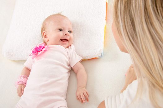 a two-month baby lying on his back on the bed, sitting next to the child and mother looking at her