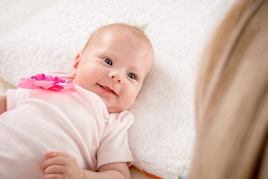 a two-month baby lying on his back on the bed, sitting next to the child and mother looking at her