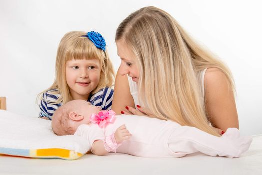 Young mother and daughter sit at the five-year crib, the crib is on a two-month baby on her back