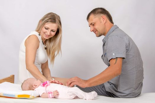 Young parents Mom and Dad sit at the crib, the crib on his back lying on the two-month girl