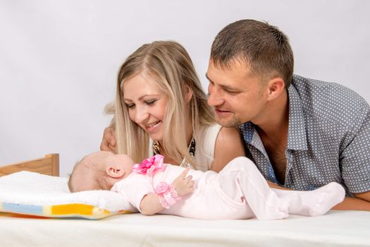 Young parents Mom and Dad sit at the crib, the crib on his back lying on the two-month girl