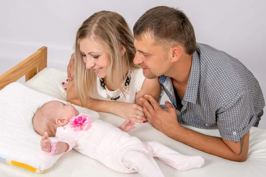 Young parents Mom and Dad sit at the crib, the crib on his back lying on the two-month girl