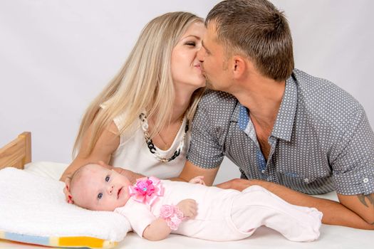 Young parents Mom and Dad sit at the crib, the crib on his back lying on the two-month girl