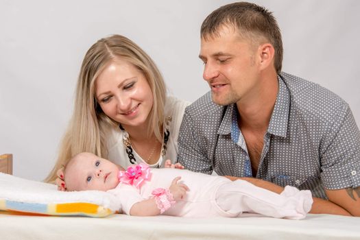 Young parents Mom and Dad sit at the crib, the crib on his back lying on the two-month girl