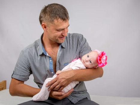Young dad sitting on a bed and holds her two-month baby daughter