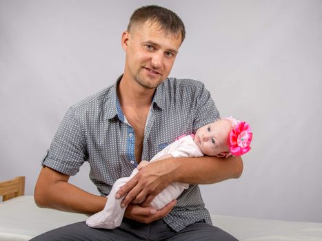 Young dad sitting on a bed and holds her two-month baby daughter
