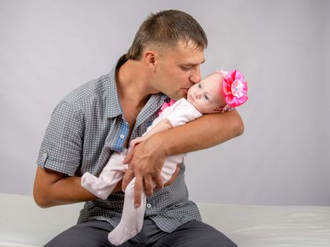 Young dad sitting on a bed and holds her two-month baby daughter