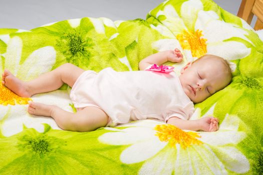 a two-month baby girl Europeans lies on a soft bed on colored coverlet