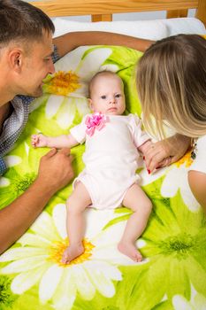 Young parents Mom and Dad sit at the crib, the crib on his back lying on the two-month girl