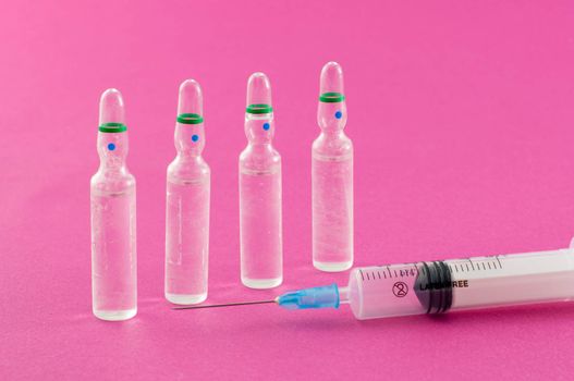 Phials and syringe on pink background