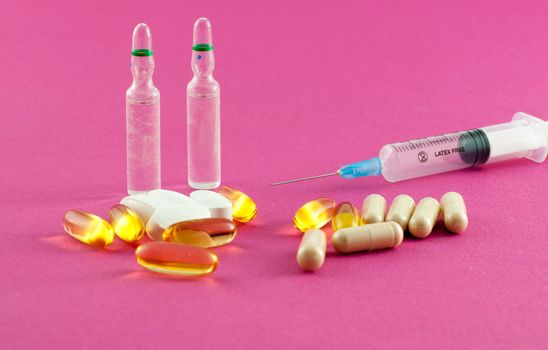 Phials, pills and syringe on pink background