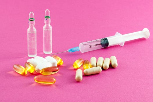 Phials, pills and syringe on pink background