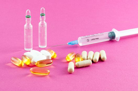 Phials, pills and syringe on pink background