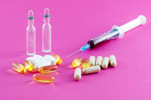 Phials, pills and syringe on pink background