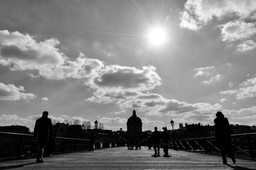 Silhouette of people walking on Pont des Arts in Paris, France. Black and white photograph.