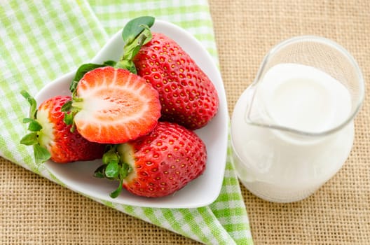 Fresh strawberries in white bowl and milk in glass on tablecloth.
