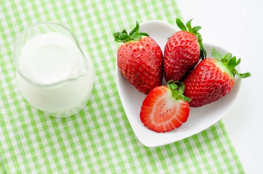 Fresh strawberries in white bowl and milk in glass on tablecloth.