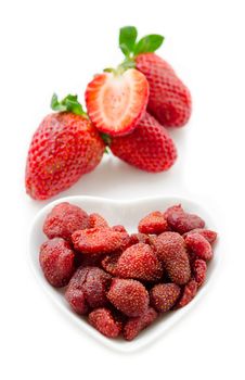 Dried strawberries in white bowl and fresh strawberry on white background.