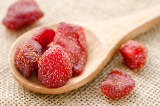 Dried strawberries in wooden spoon on sack background.