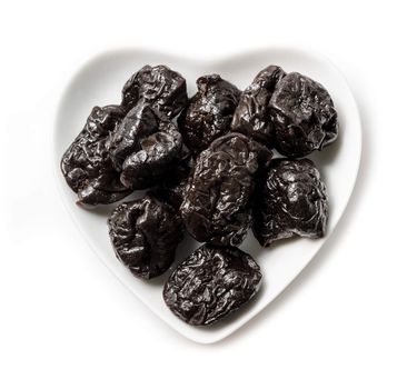 Dried Prunes in white bowl heart shape on white background.