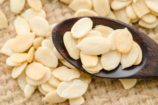 Crack shell watermelon seeds in wooden spoon on sack background.